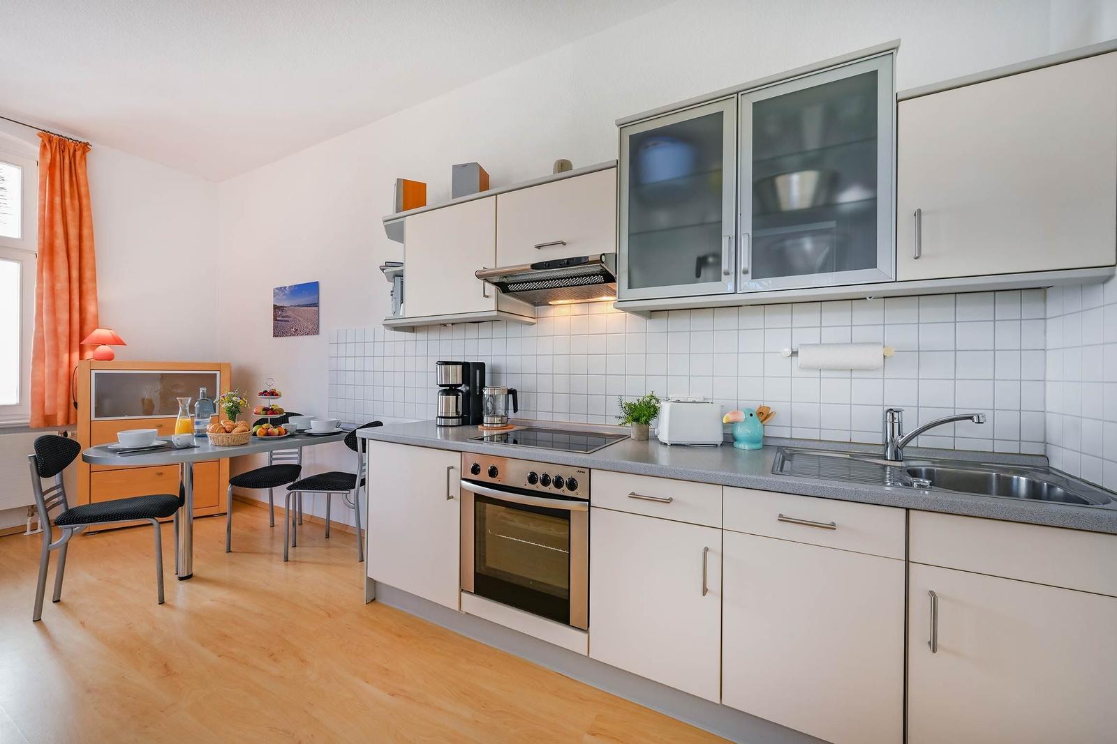 Küche mit Arbeitsplatte, Spüle und Kochfeld. Essbereich mit Tisch und Stühlen.