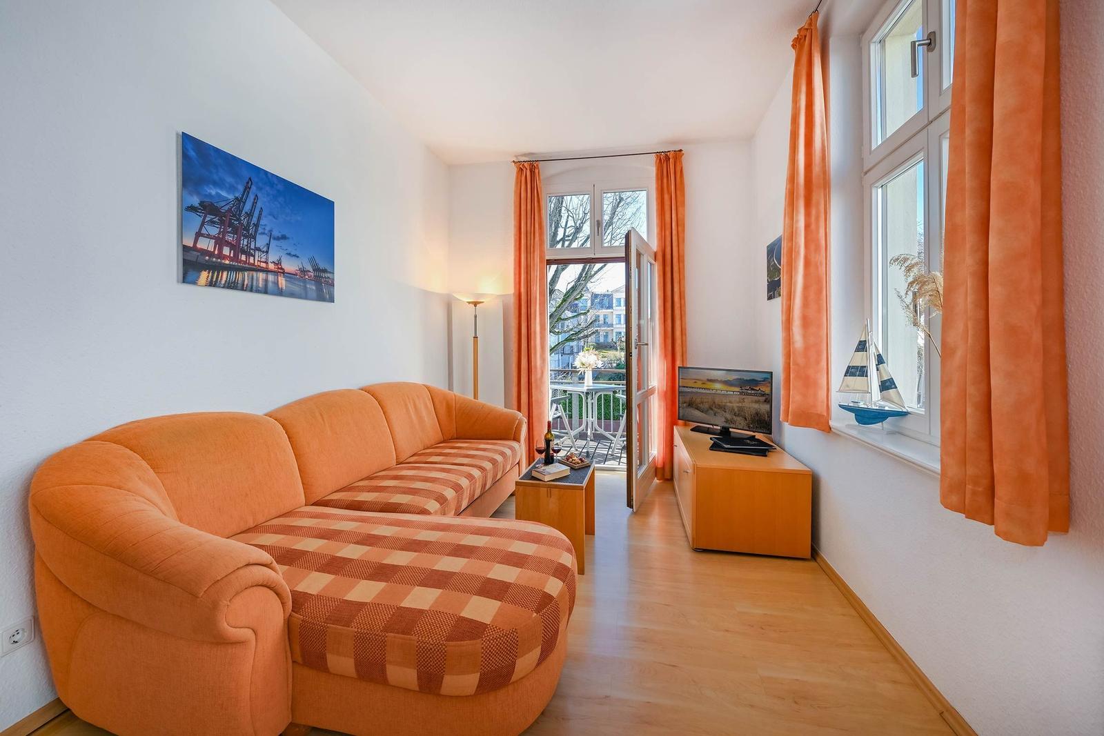 Wohnzimmer mit orangefarbenem Sofa, Holzboden und Blick auf Balkon.