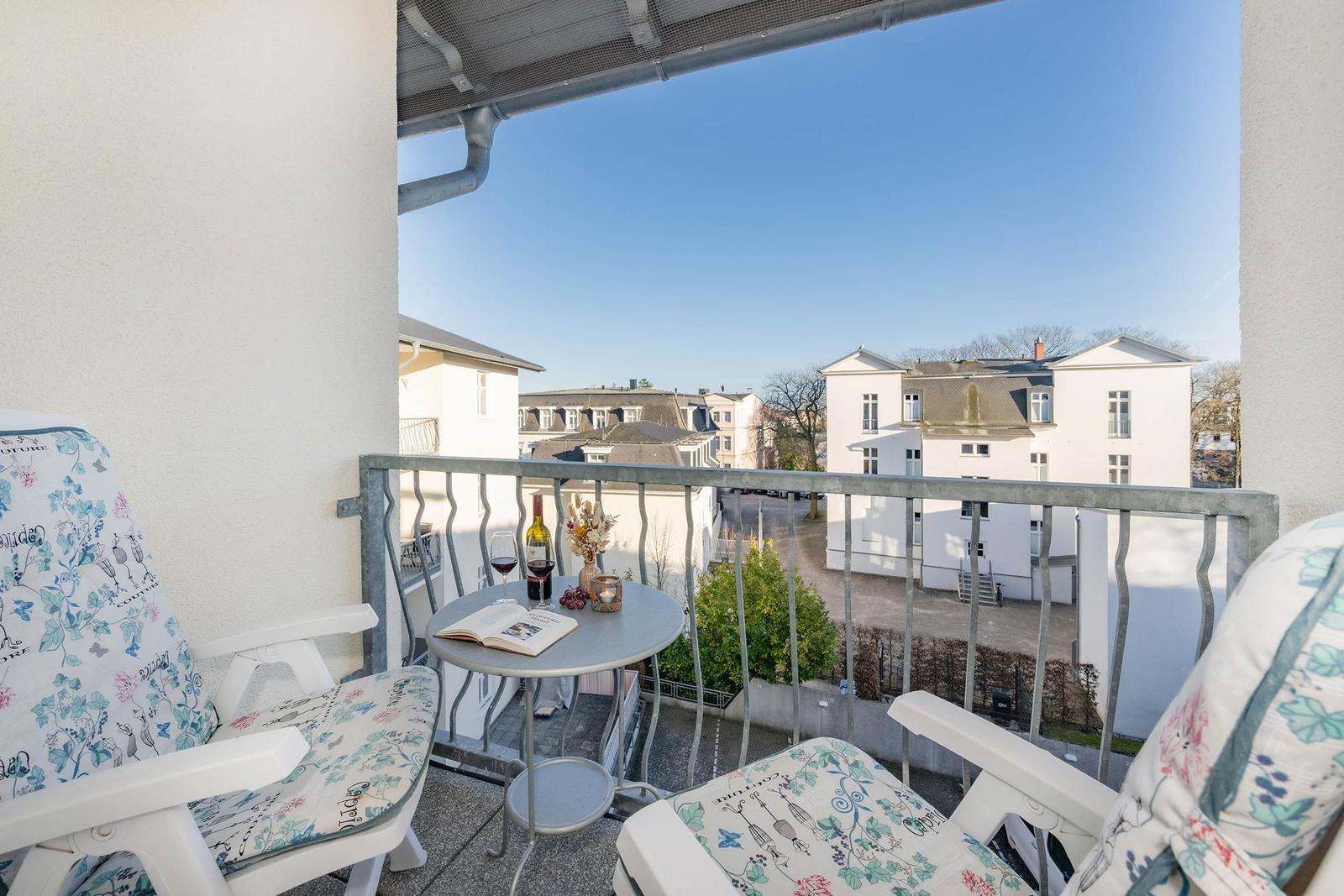 Balkon mit zwei Stühlen, Tisch und Blick auf Gebäude.