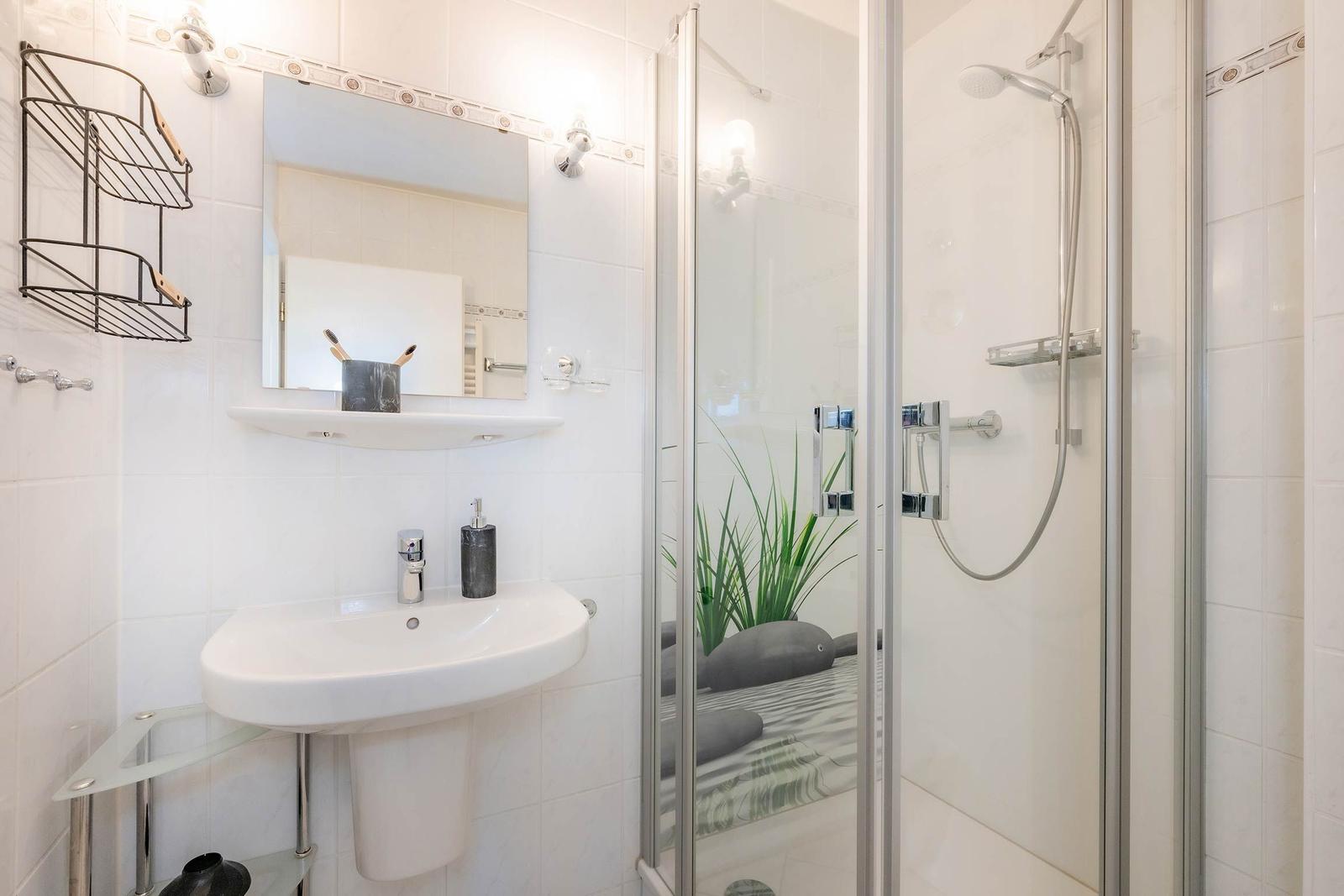 Badezimmer mit Dusche, Waschbecken und Spiegel.