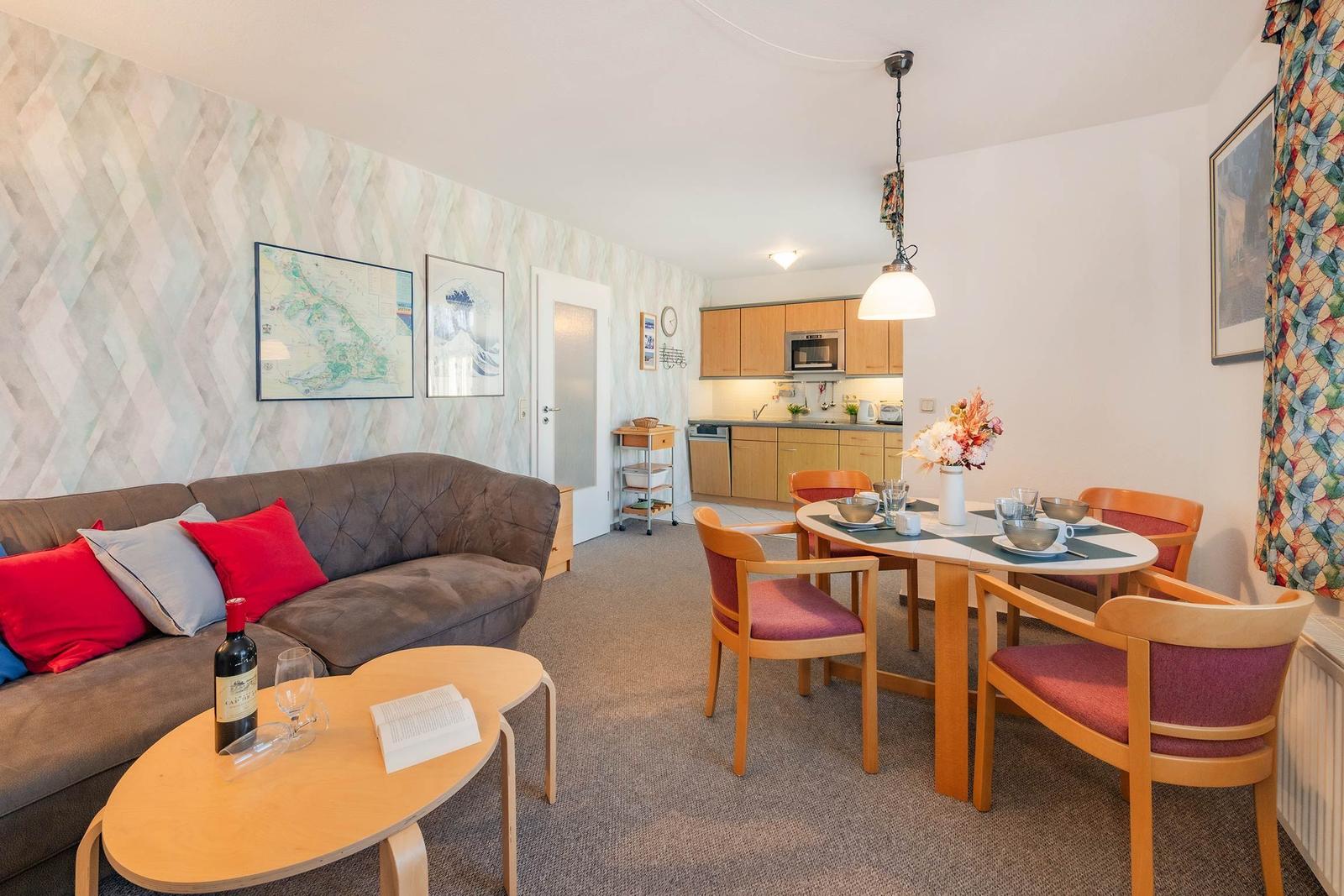 Wohnzimmer mit Sofa, Esstisch und Küchenbereich im Hintergrund.