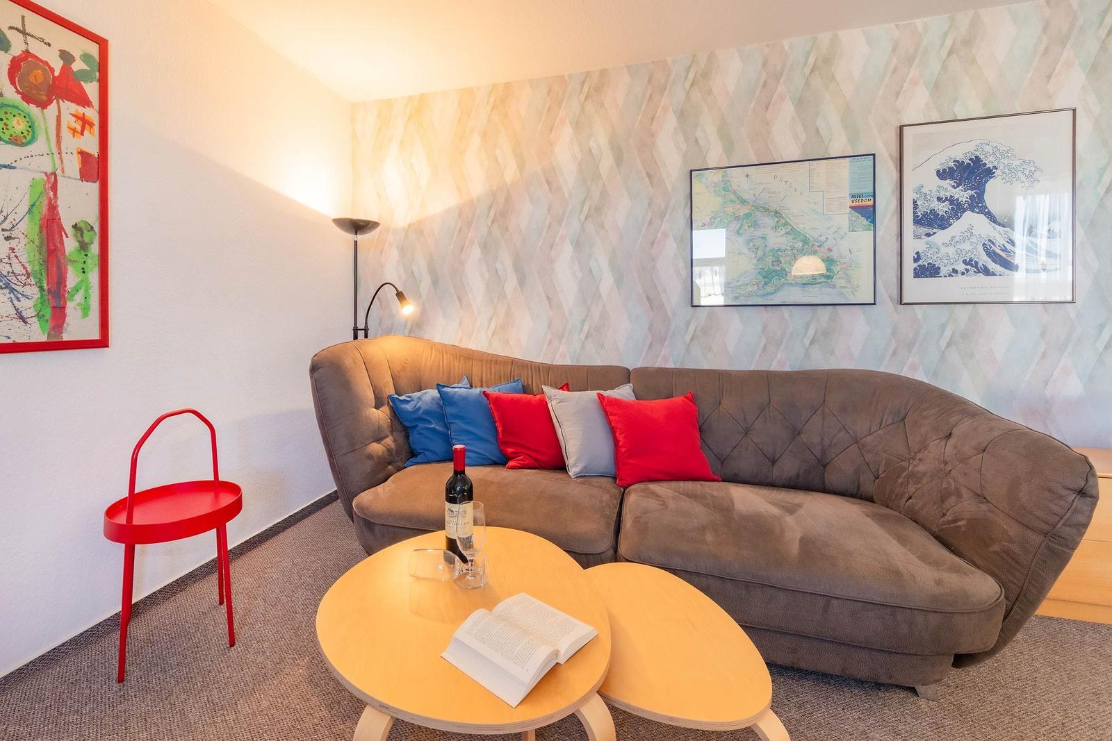 Ein Wohnzimmer mit braunem Sofa, rotem Stuhl und Karten an der Wand.