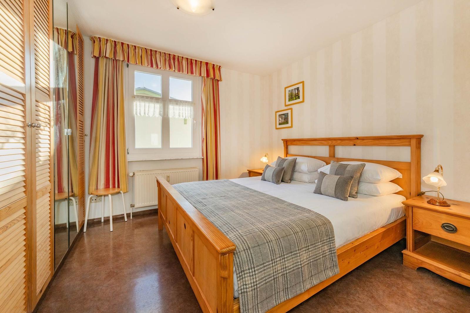 Ein Schlafzimmer mit Holzbett, Nachttischen und Fenster mit Vorhängen.