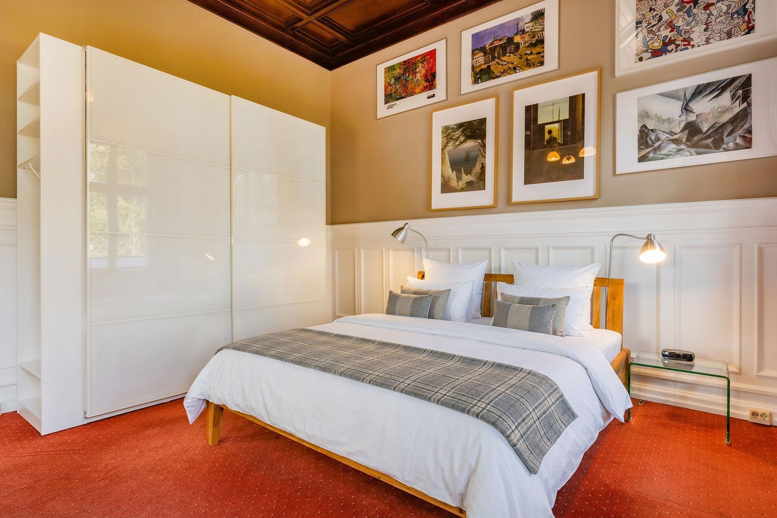 Schlafzimmer mit Bett, Kleiderschrank und Wandbildern.