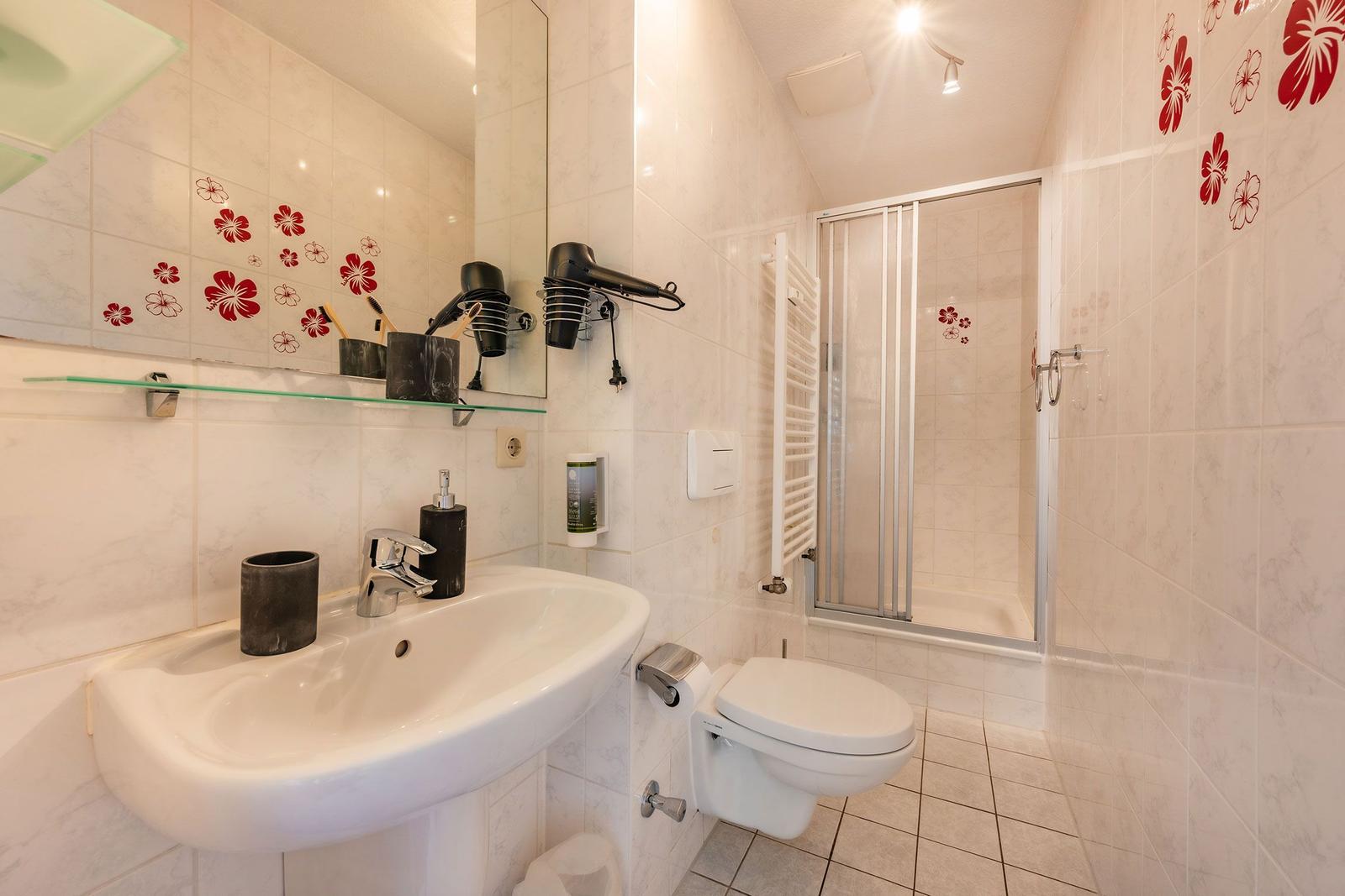 Badezimmer mit Dusche, Waschbecken und Toilette. Wandfliesen mit roten Blumenmotiven.