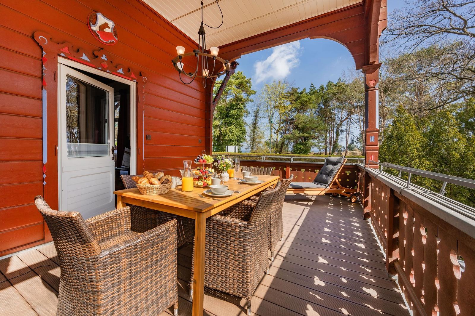 Terrasse mit Esstisch, Stühlen und Blick auf Wald. Holzhaus mit weißen Türen.