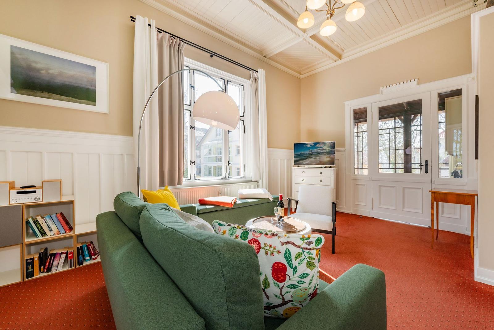 Ein Wohnzimmer mit grünem Sofa, rotem Teppich und TV. An der Wand hängt ein Bild.