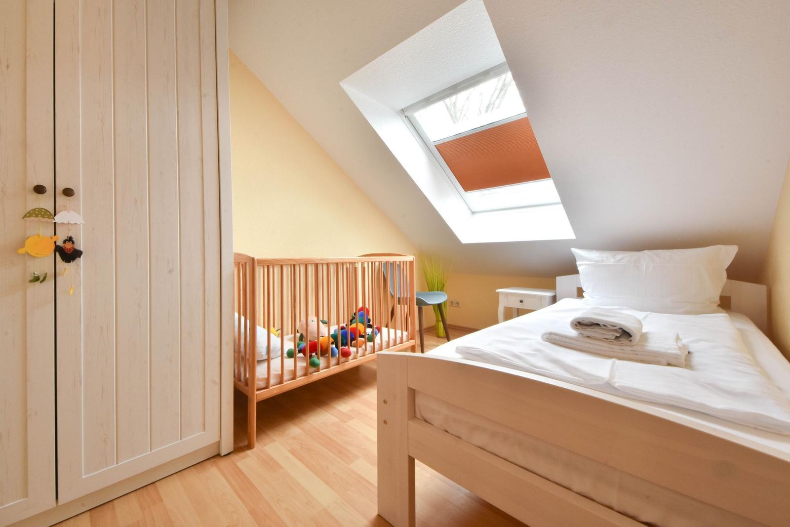 Schlafzimmer mit Babybett und Dachschiebefenster. Holzboden und Kleiderschrank.