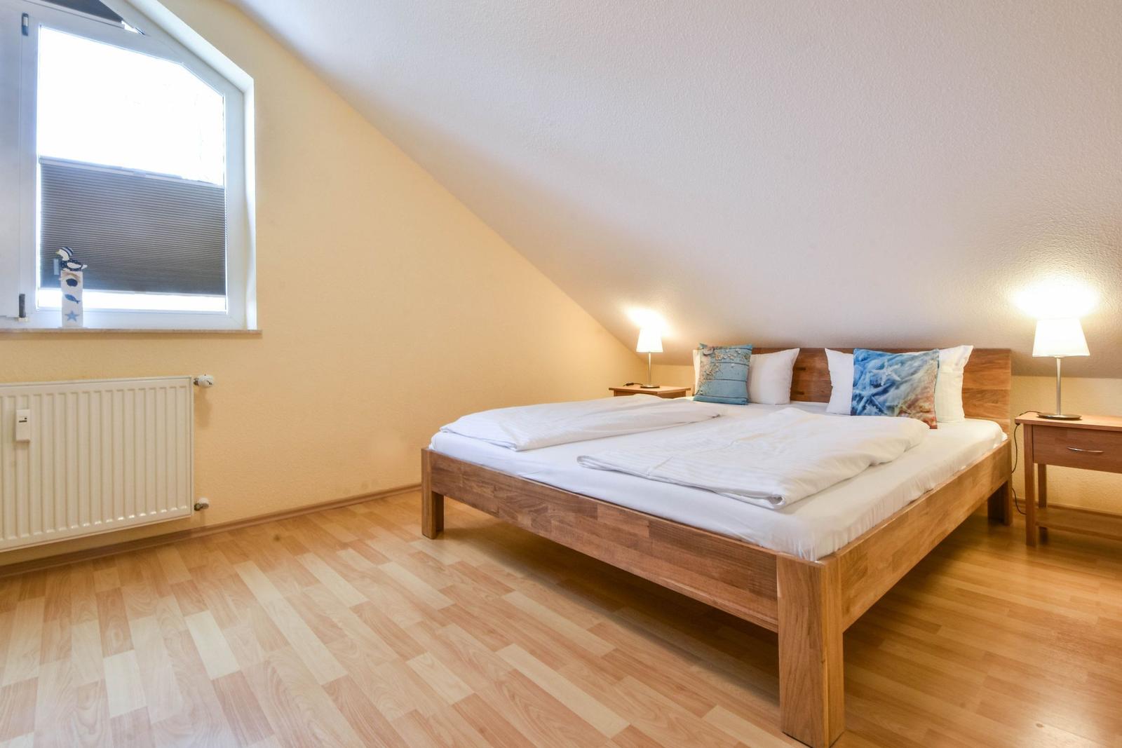 Schlafzimmer mit Holzbett, zwei Nachttischen und Fenster mit Jalousie.