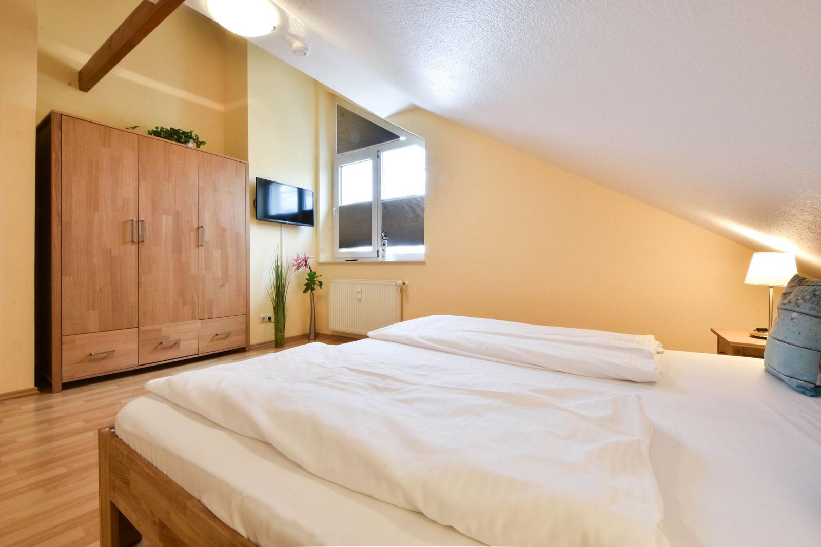Schlafzimmer mit Doppelbett, Holzmöbel und Fenster. Decke geneigt.