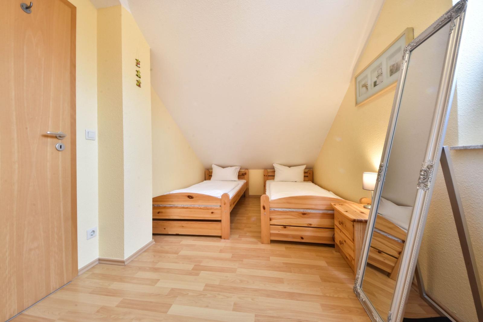 Zwei Einzelbetten, Holzmöbel und Spiegel in einem Dachzimmer mit Holzboden.