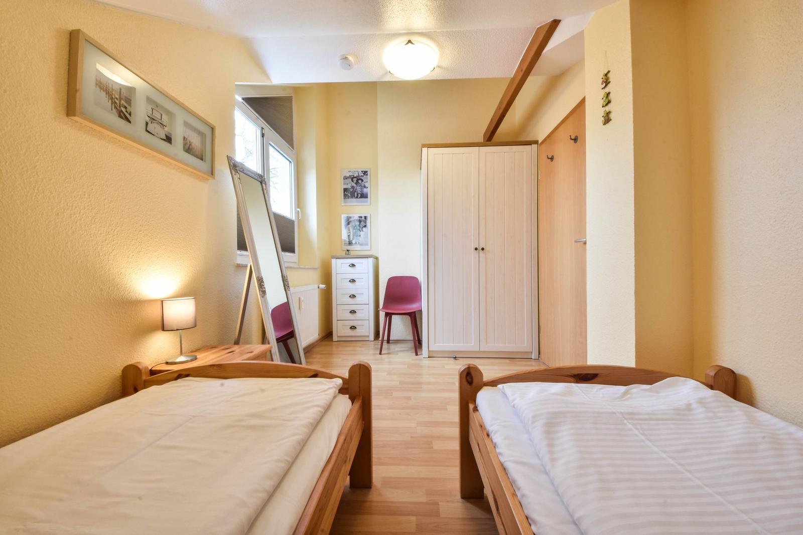 Zwei Einzelbetten, Kleiderschrank, Spiegel und Fenster im Schlafzimmer.