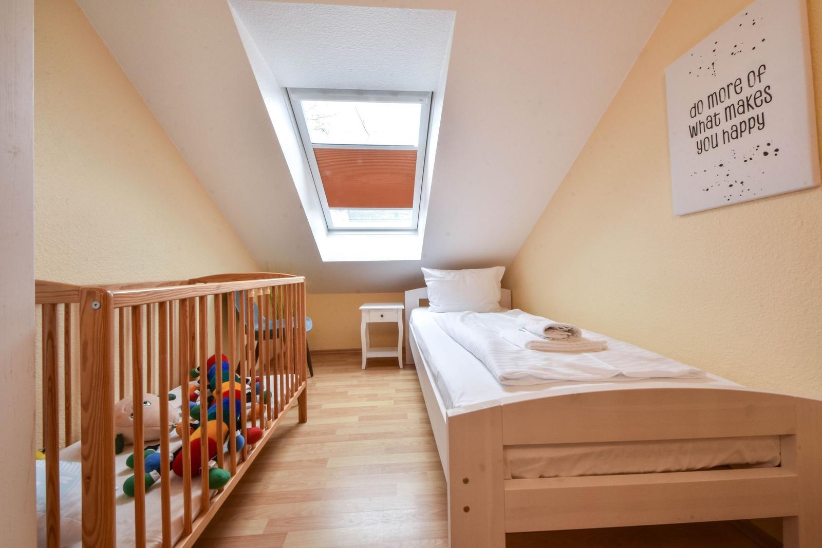 Schlafzimmer mit Babybett, Einzelbett und Dachfenster.