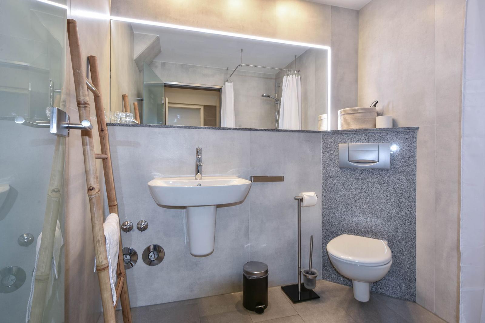 Badezimmer mit Waschbecken, Toilette und Dusche. Spiegel mit LED-Beleuchtung.