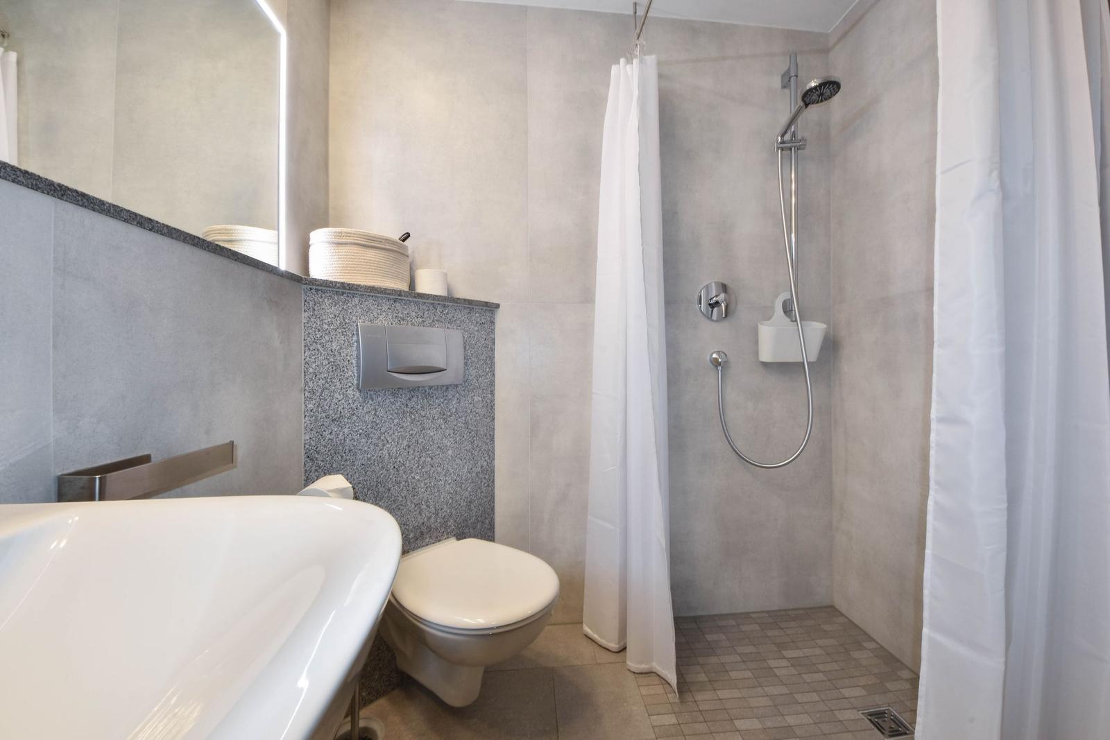 Bad mit Dusche, Toilette und Waschbecken. Duschbereich mit Duschbrause und Vorhang.
