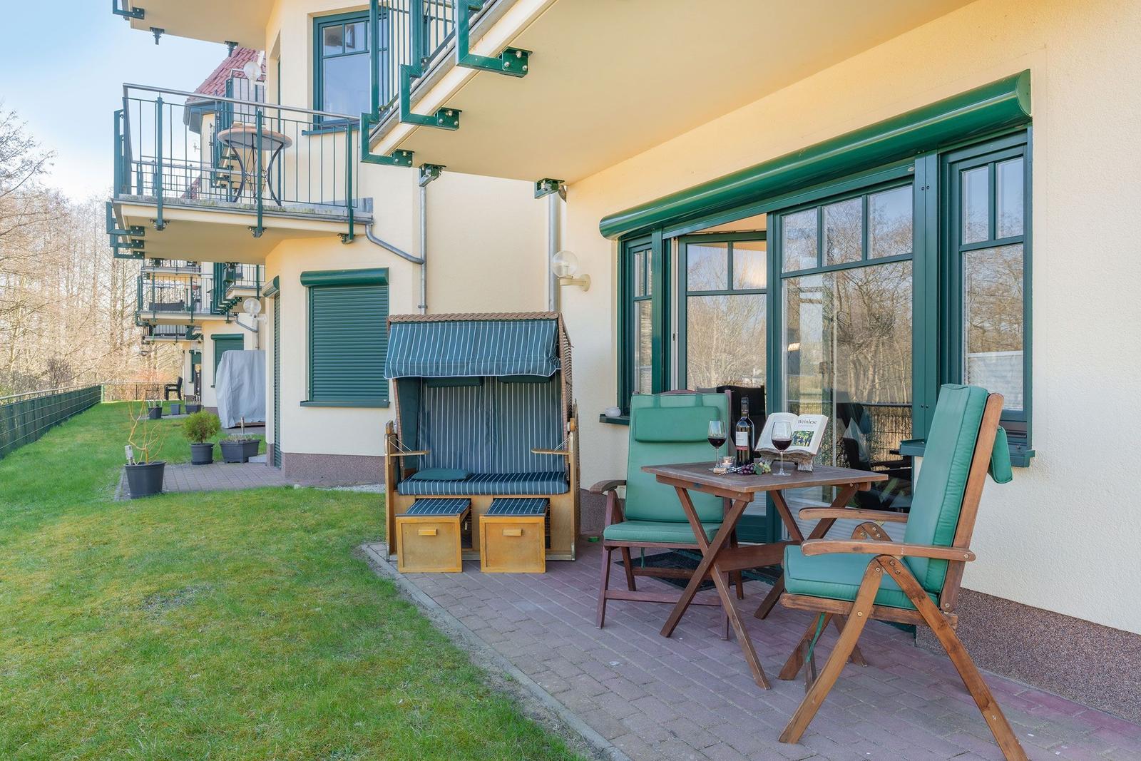Terrace with seating group, beach chair, and table. Green-framed windows and yellow stucco.