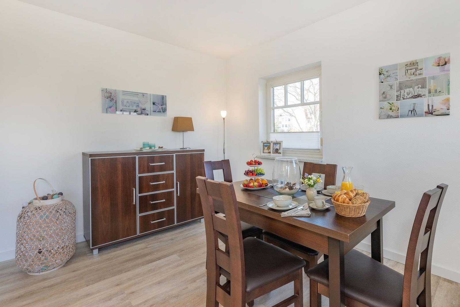 Dining table with chairs, cabinet, and window. Fruit and bread on the table.