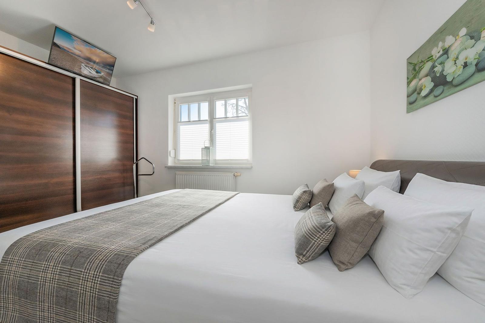 Bedroom with bed, window, and wardrobe. Wall art and bedding are visible.