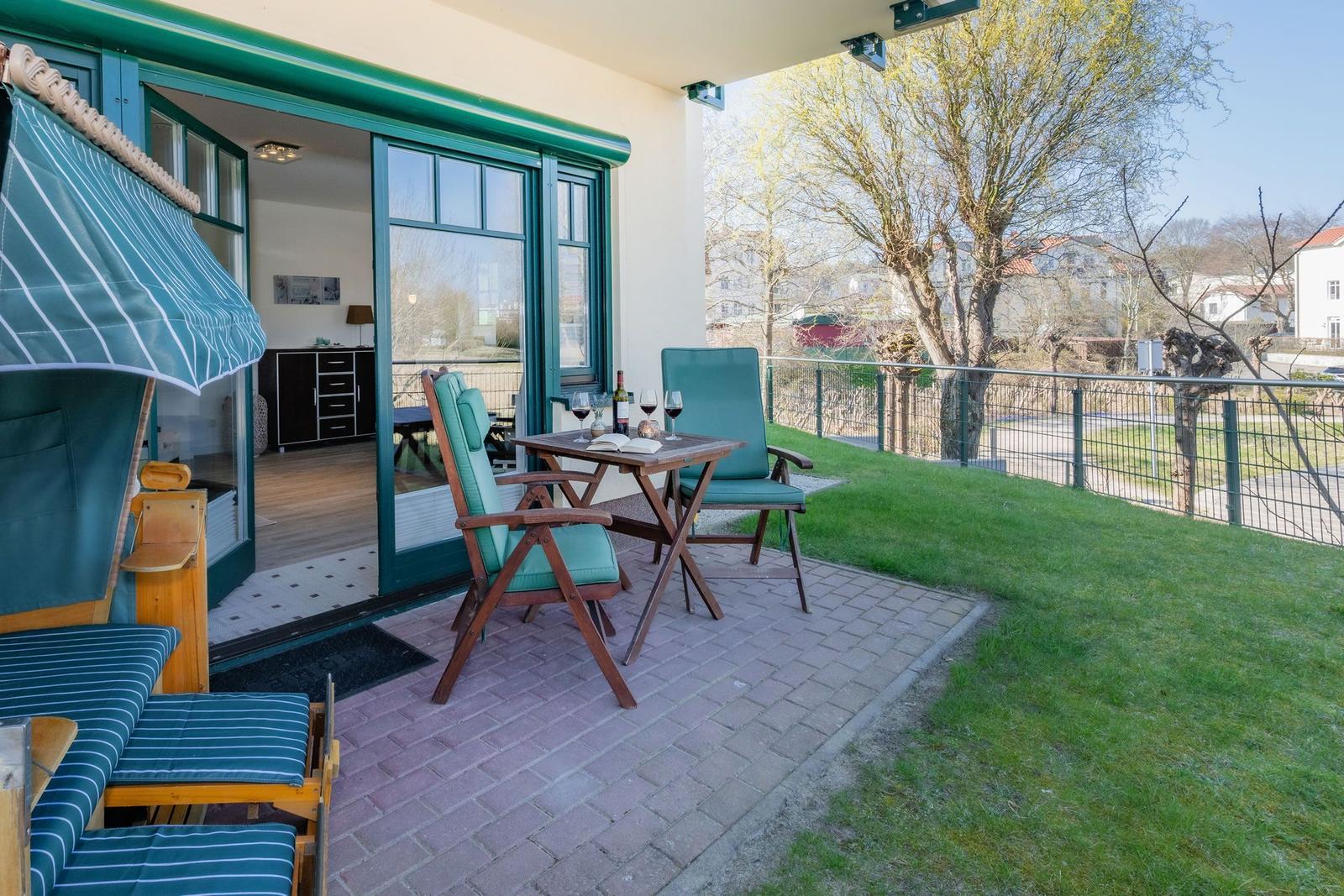 Terrace with table, two chairs, and lounge chair. Glass doors lead to the interior.