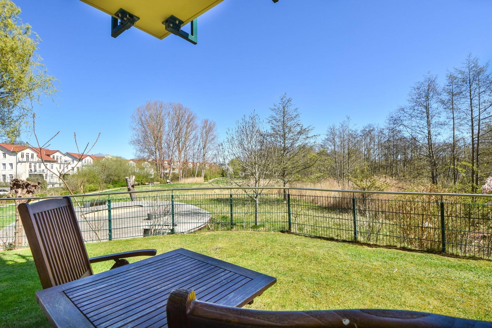 Terrace with table and chairs, view of green area and trees.
