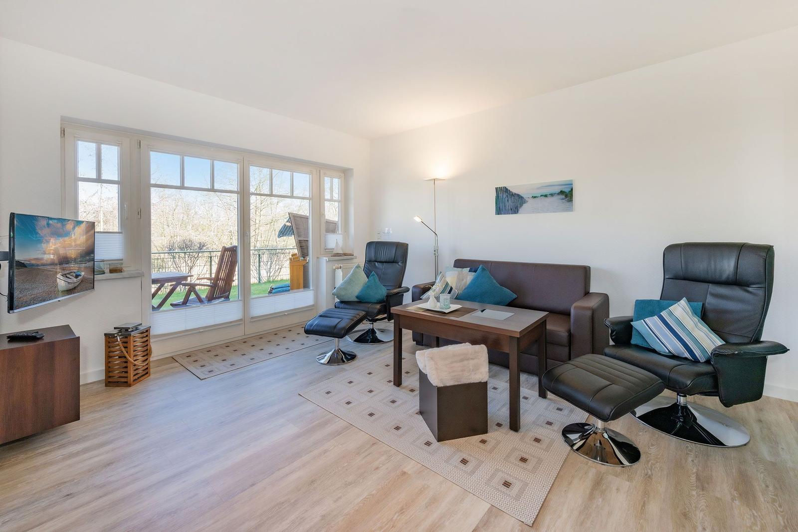 Living room with sofa, two chairs, and TV. Large windows with view of balcony.