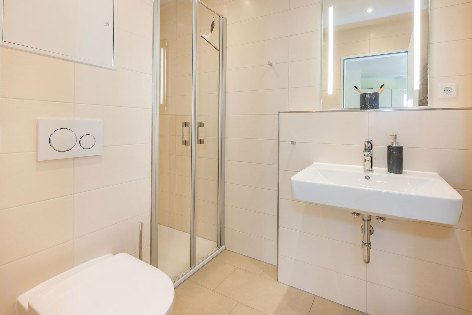 Bad mit Dusche, Waschbecken und Toilette. Fliesenwand und Spiegel.