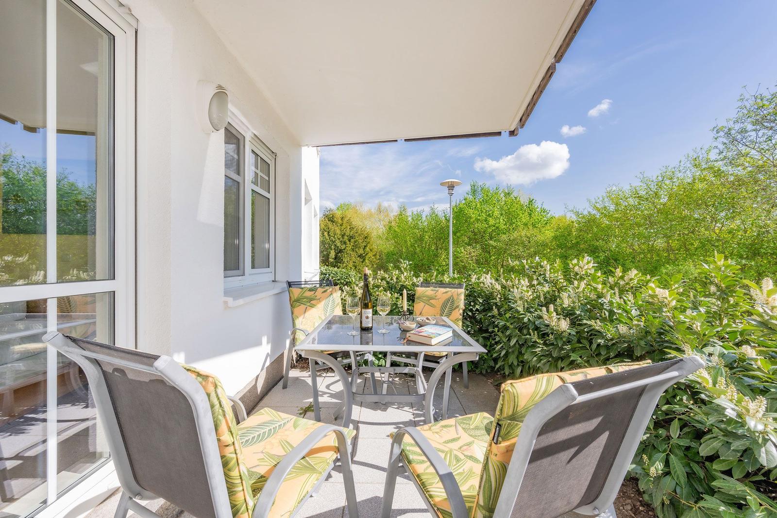 Terrasse mit Tisch und Stühlen, umgeben von Grünflächen und einem klaren Himmel.