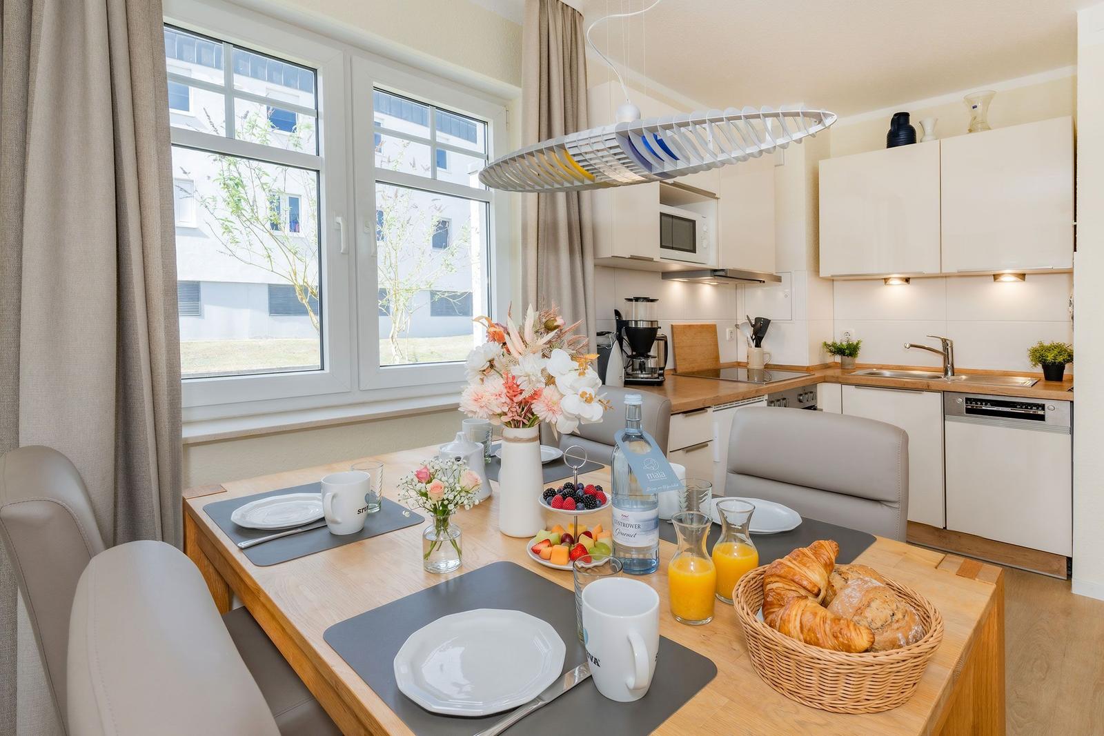 Essbereich mit Tisch, Stühlen und Frühstück. Küchenzeile mit Spüle, Kühlschrank und Kochfeld.