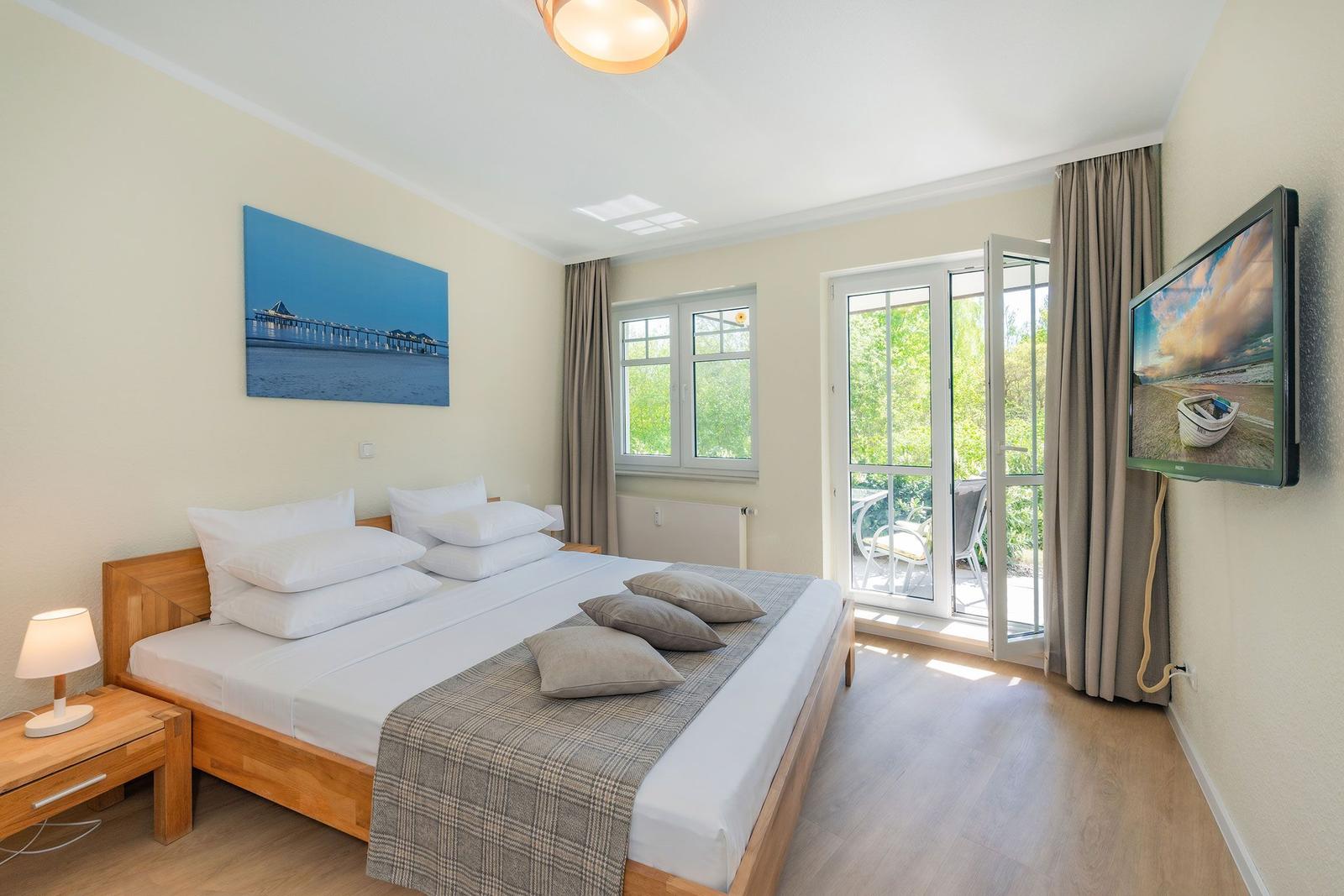 Schlafzimmer mit Doppelbett, TV und Balkon. Wandbild und Holzmöbel.