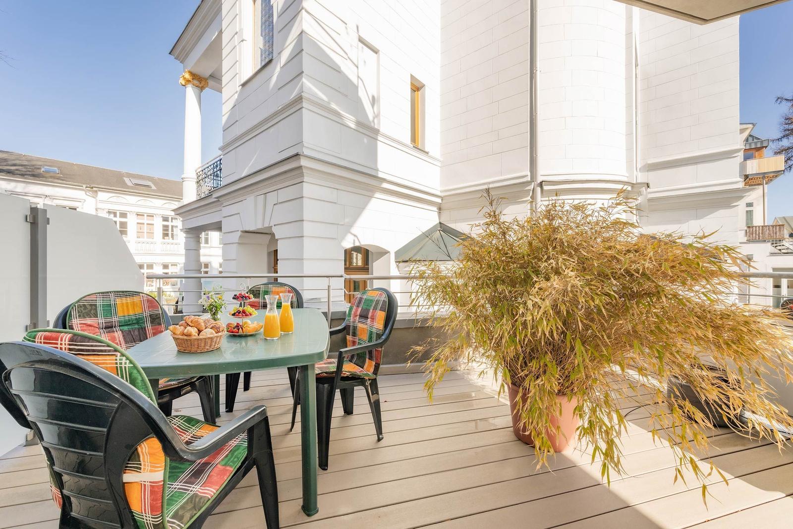 Terrasse mit Tisch, Stühlen und Pflanze vor weißem Haus