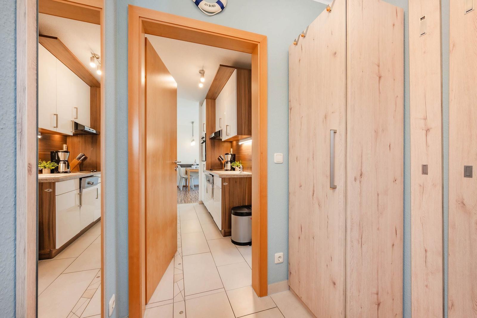 Flur mit Holzschrank, Blick in Küche und Essbereich mit Küchenschränken.