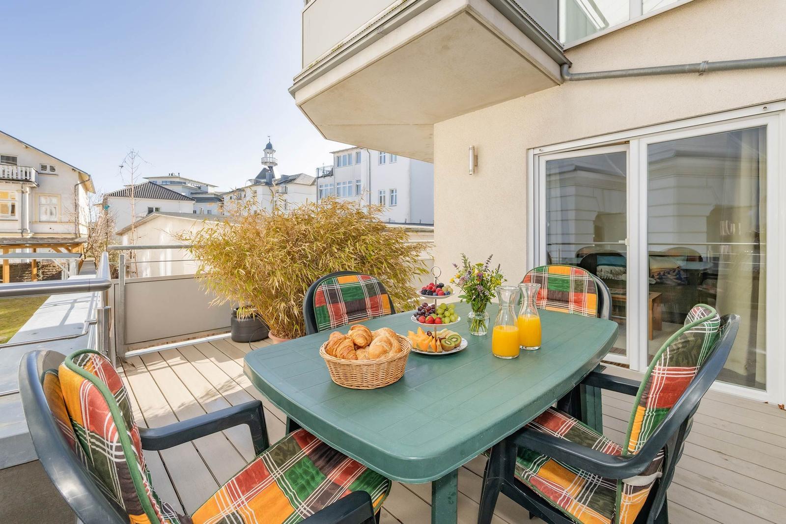 Terrasse mit Tisch, Stühlen und Frühstück. Blick auf Gebäude und Bäume.