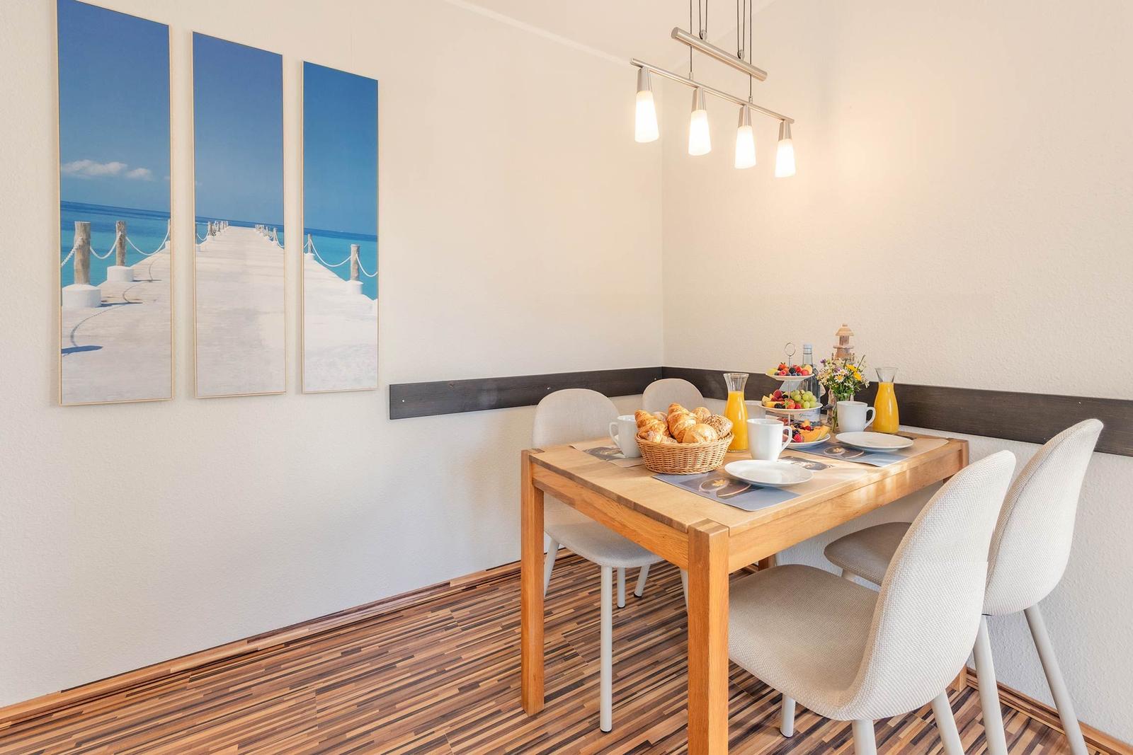 Essbereich mit Holztisch, Stühlen und Frühstück. Wandbild zeigt Strand.
