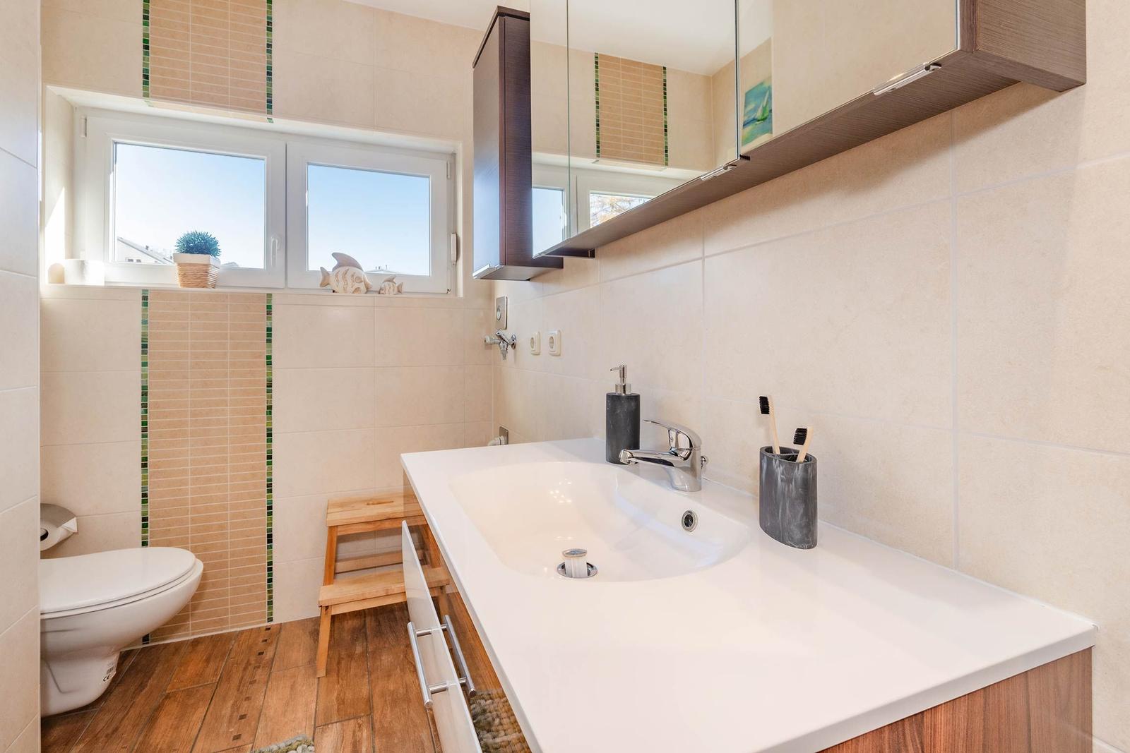 Bad mit Waschbecken, Spiegel, Toilette und Fenster mit Blick nach draußen.