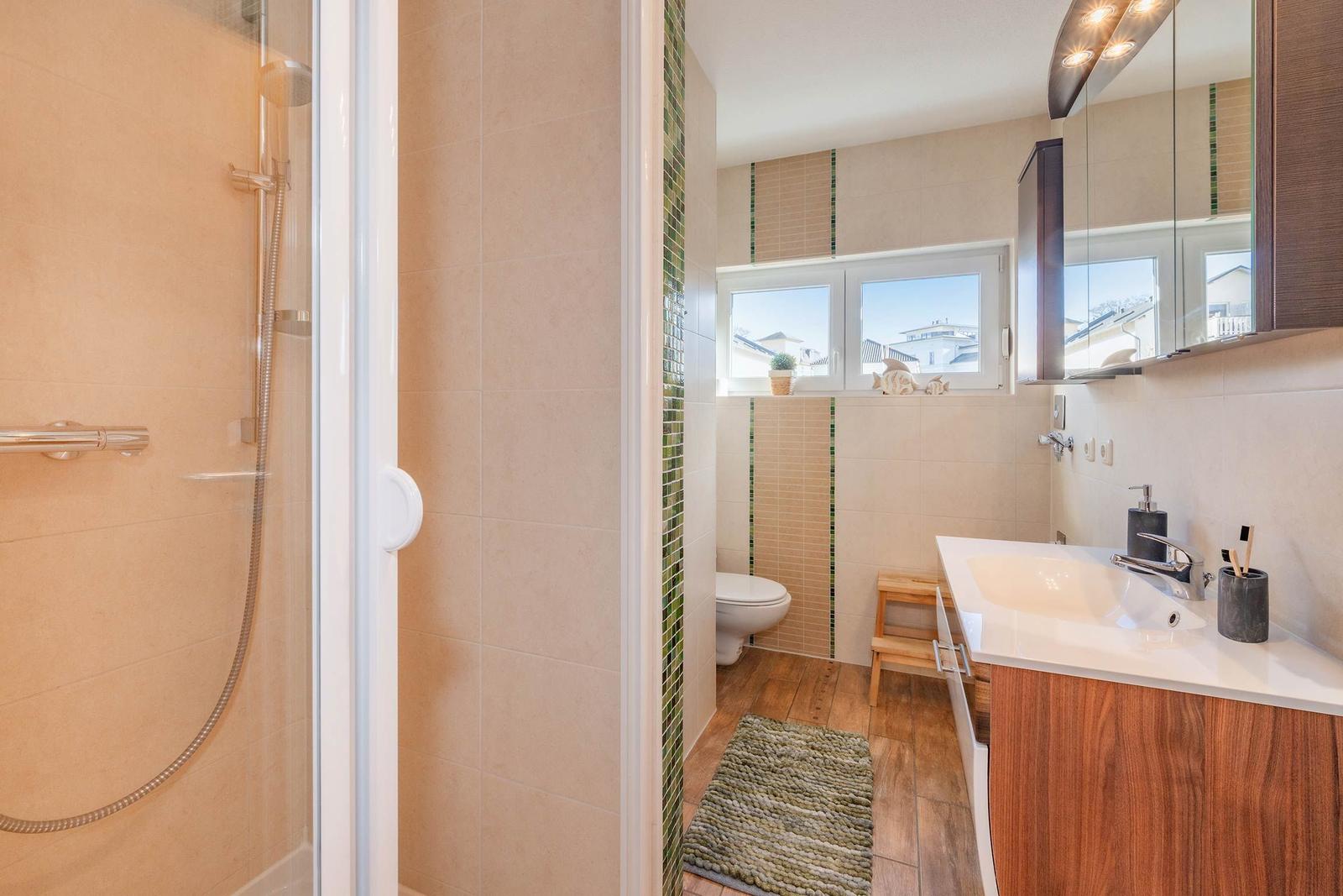 Badezimmer mit Dusche, Waschbecken und Toilette. Holzfußboden und Fenster mit Blick.