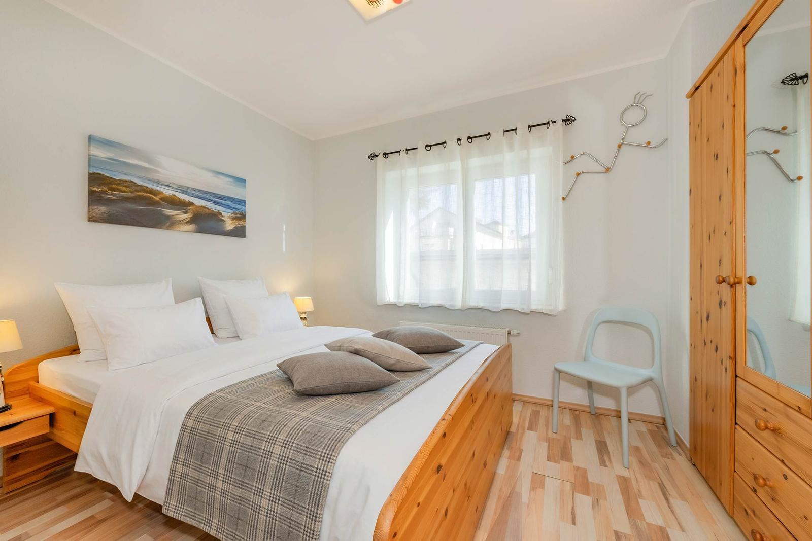 Schlafzimmer mit Doppelbett, Holzmöbeln und Fenster mit Vorhängen.