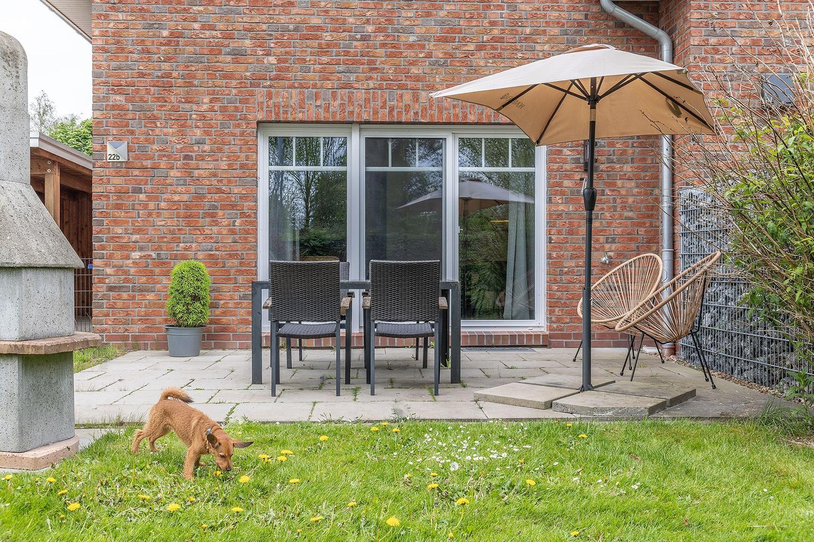 Terrace with seating, umbrella, and garden. A dog sniffs the grass.