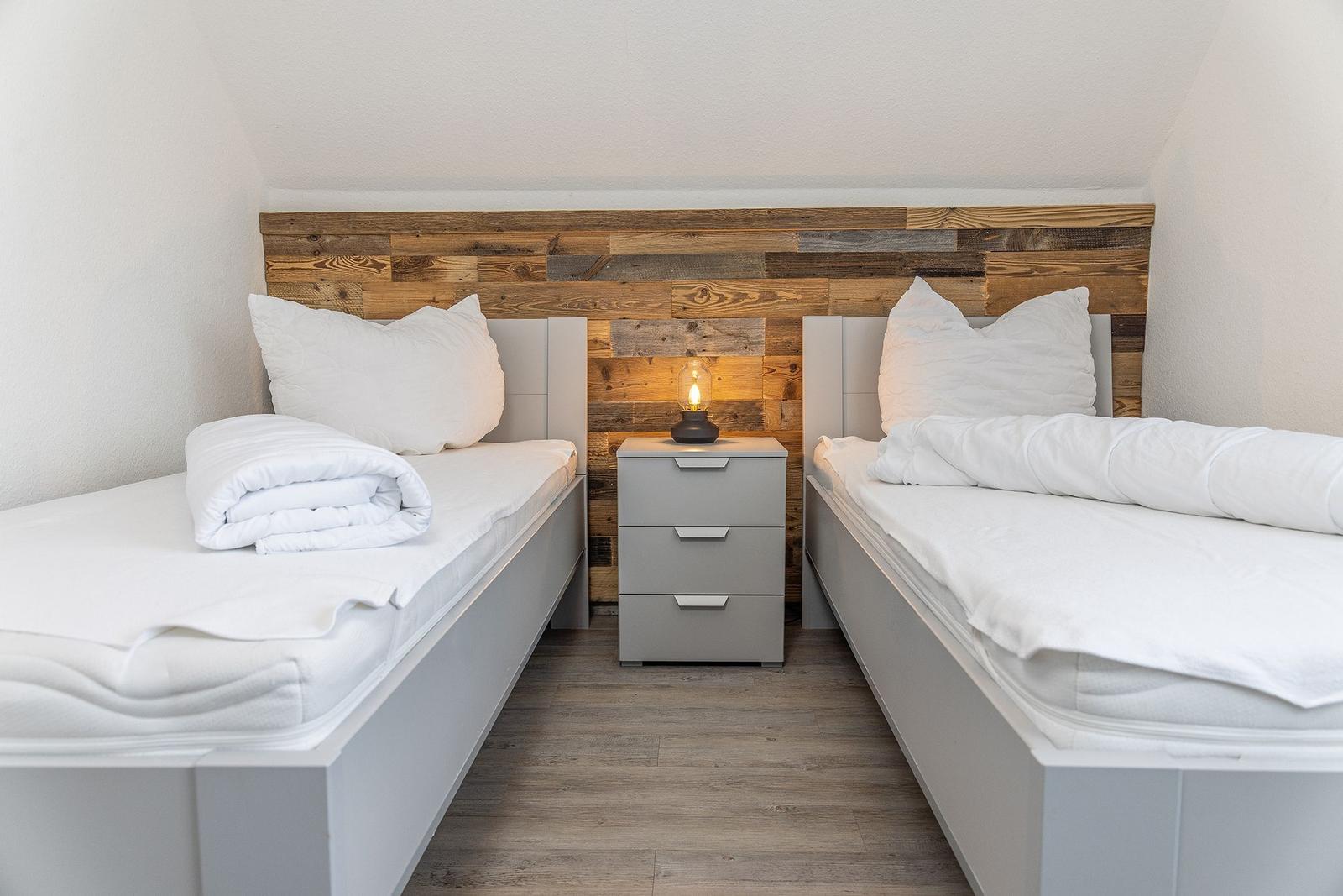 Two beds with white linens and wooden panels on the wall.