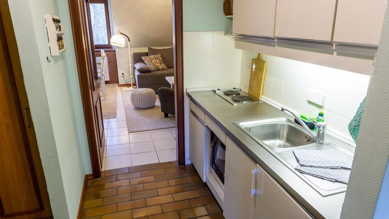 Küche mit Spüle, Herd und Küchenschränken. Durchgang zum Wohnzimmer mit Sofa und Beistelltisch.