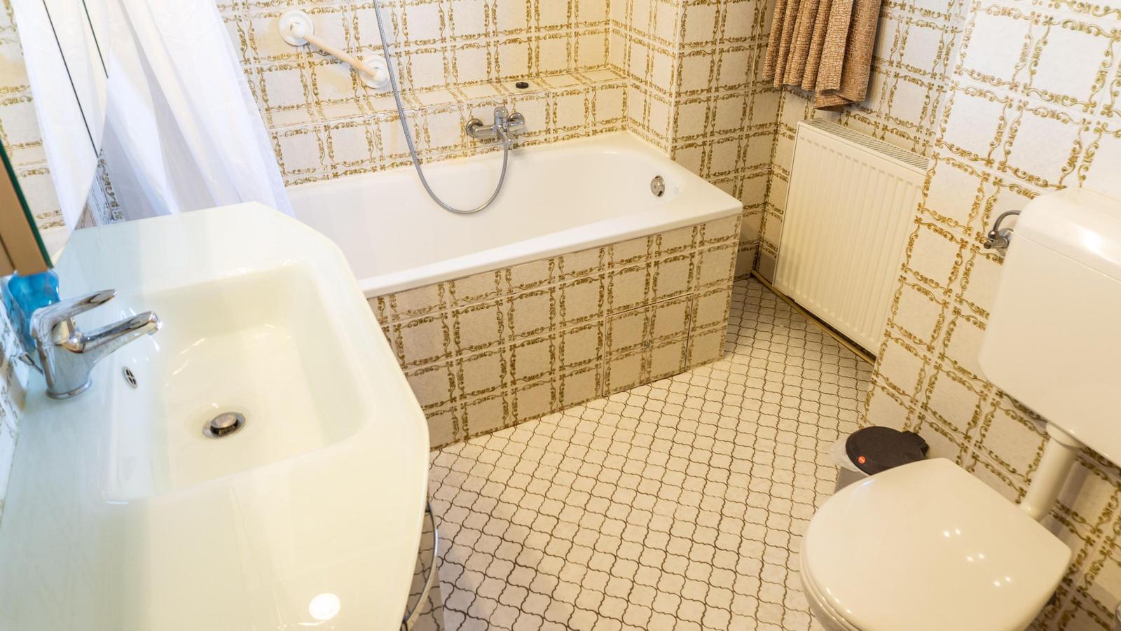 Badezimmer mit Badewanne, Waschbecken und Toilette. Fliesen mit goldfarbenem Muster.