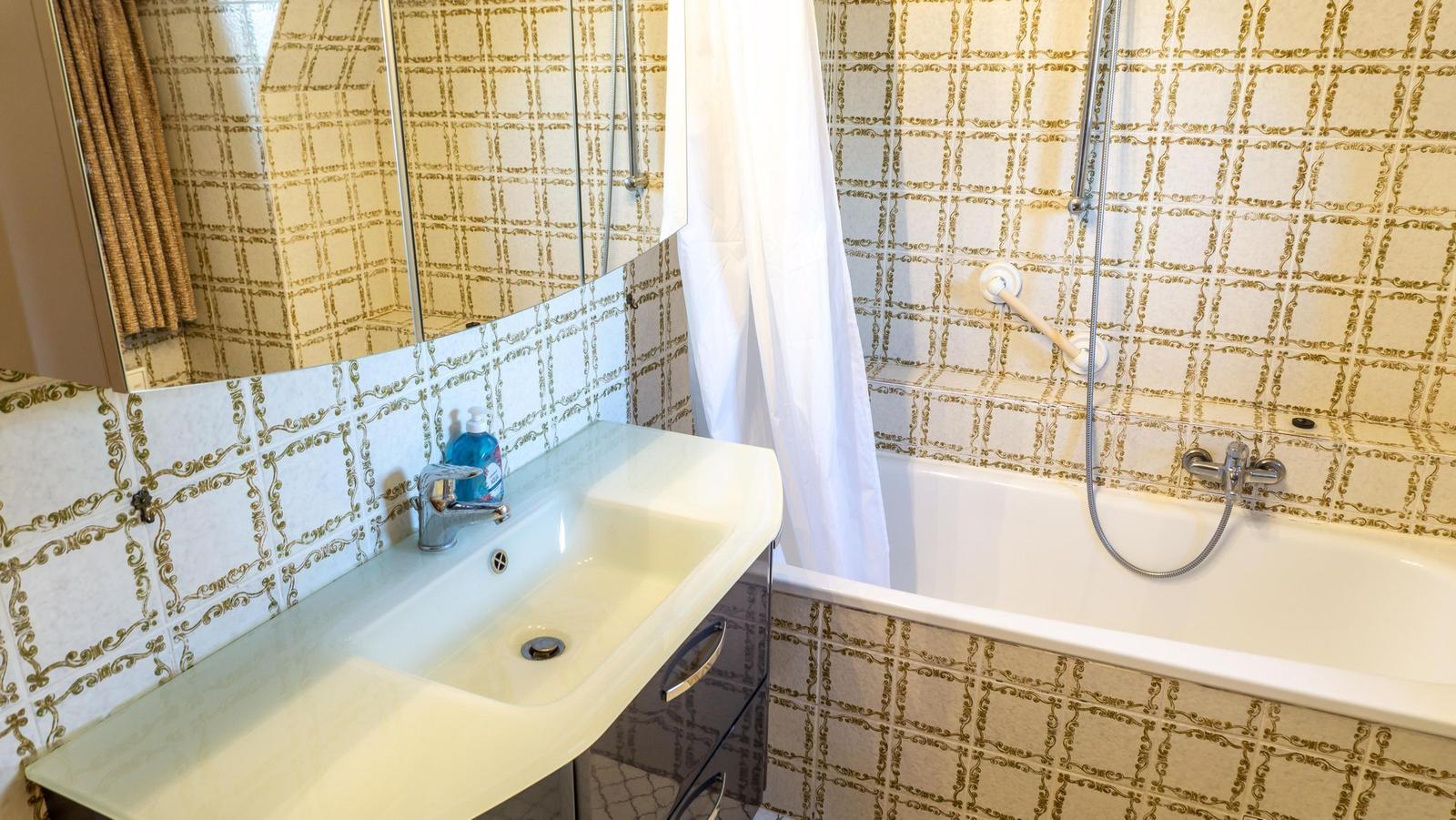 Badezimmer mit Waschbecken, Dusche und Badewanne. Wandfliesen mit goldfarbenem Muster.