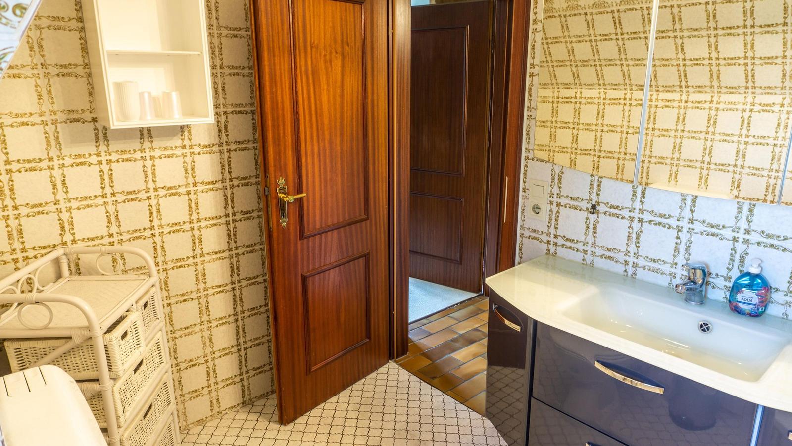 Badezimmer mit Waschbecken, Spiegelschrank und Holztüren. Wandverkleidung mit Muster.