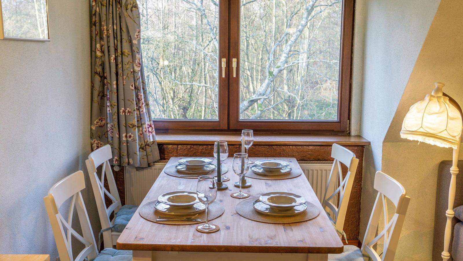 Esszimmer mit Holztisch, weißen Stühlen und Blick auf Wald durch Fenster.