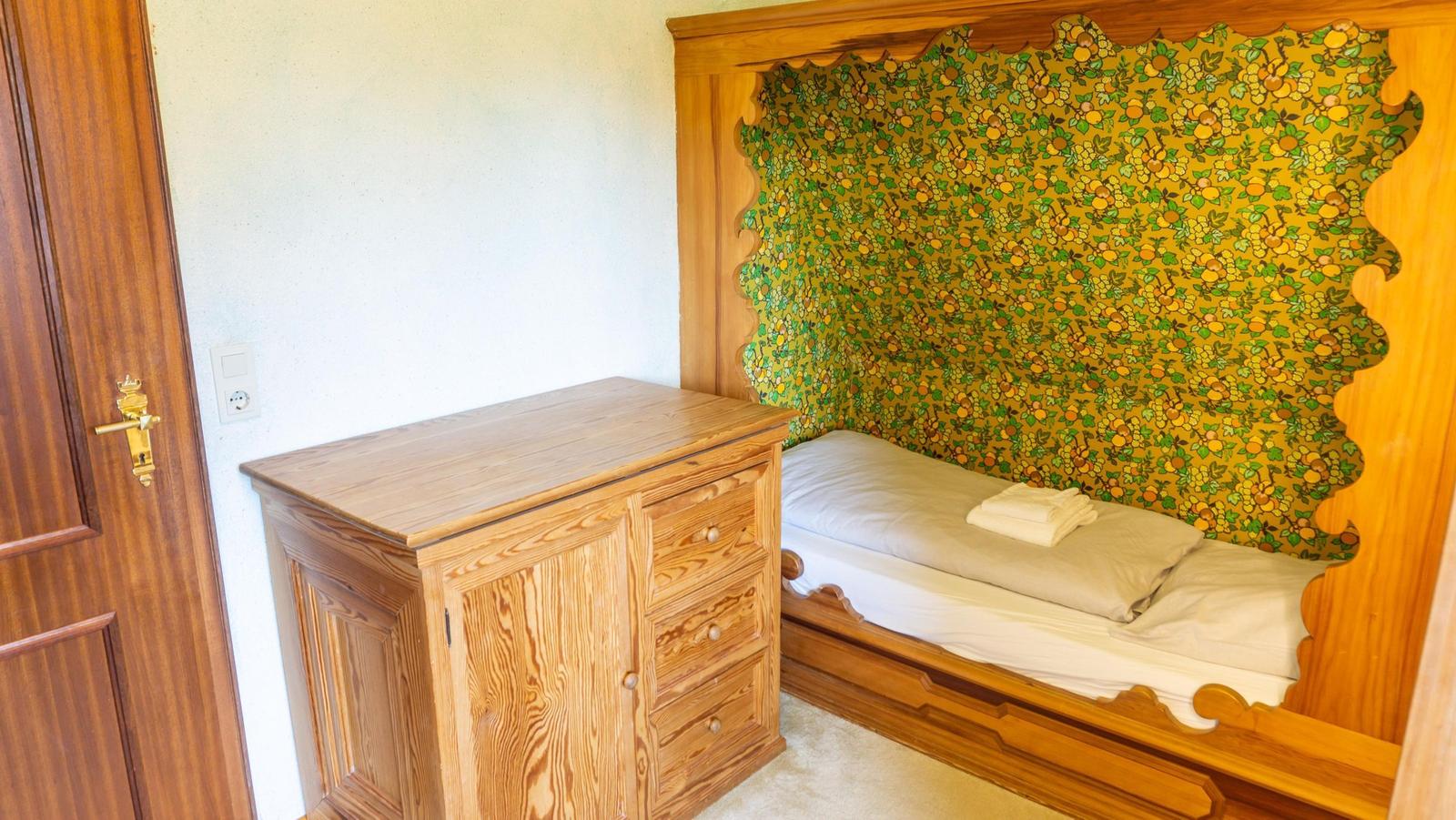 Schlafzimmer mit Holzbett und Schrank. Wandverkleidung mit Obstmotiv.