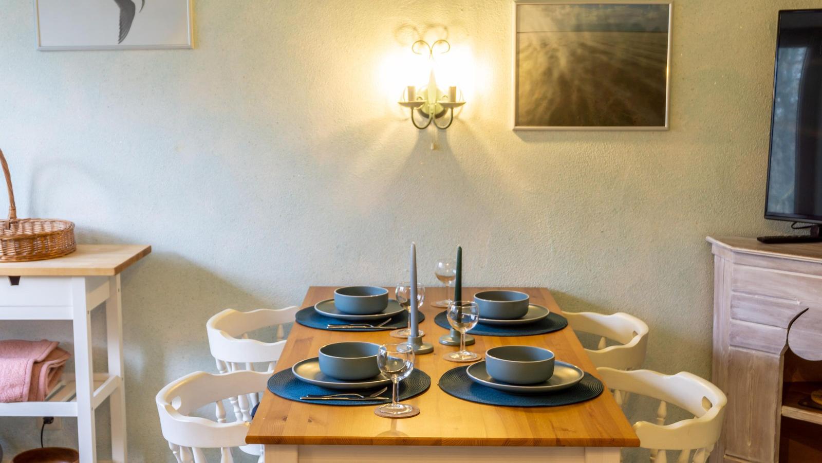 Esstisch mit vier Stühlen, Teller und Gläsern. Wandbeleuchtung und Bilder an der Wand.