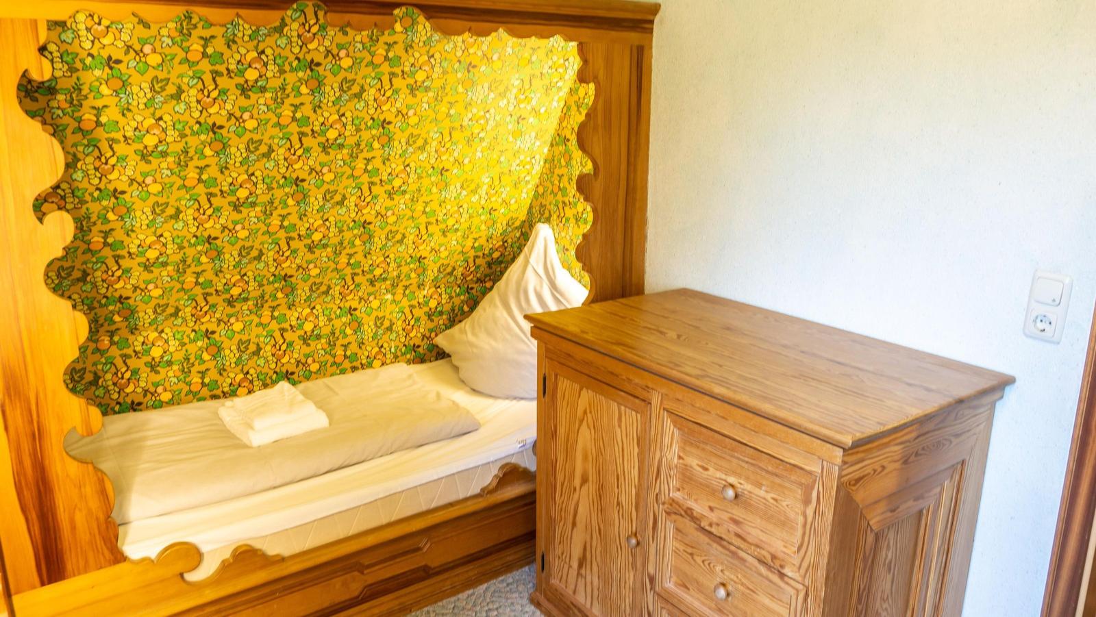 Schlafzimmer mit Holzbett und Schrank. Wandverkleidung mit Fruchtmotiv.