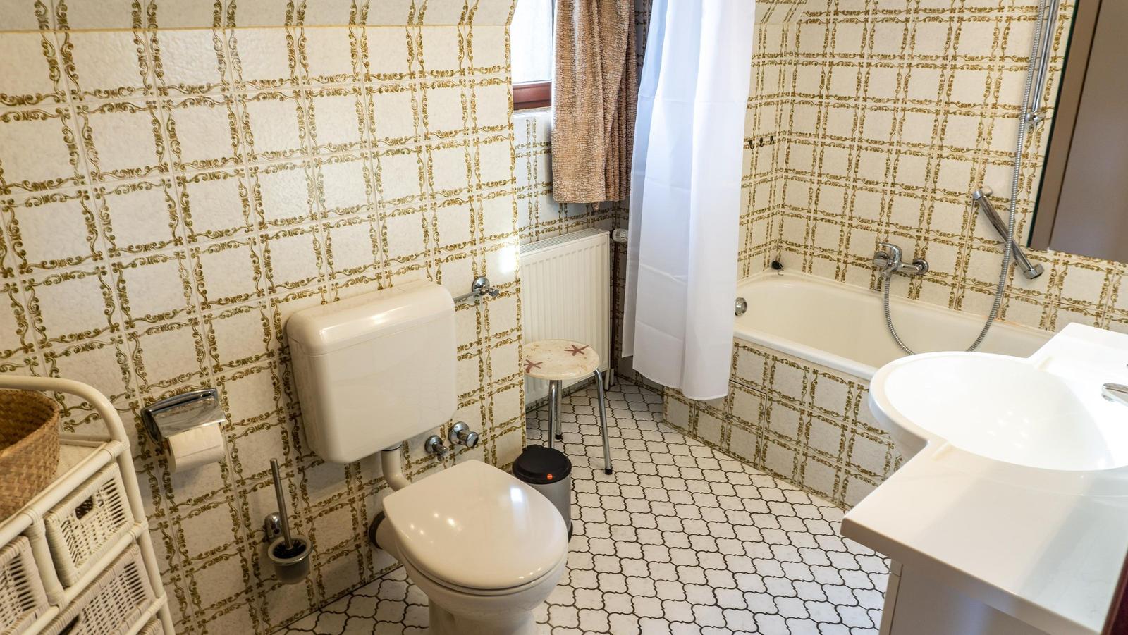 Badezimmer mit Toilette, Badewanne und Waschbecken. Wände und Boden mit Mosaikfliesen.