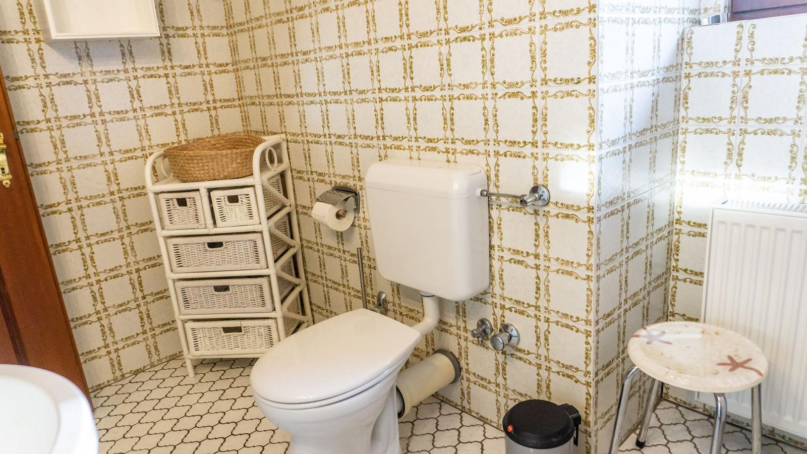 Badezimmer mit Toilette, Waschbecken und Stuhl. Wände mit goldfarbenem Muster.
