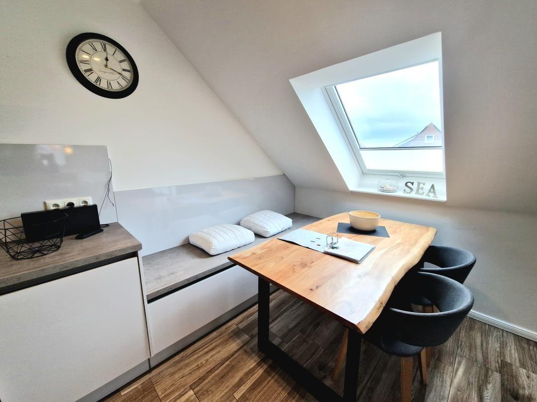 Dachgeschosszimmer mit Schlafcouch, Tisch und Sitzgelegenheit. Fenster zeigt Blick auf Haus.