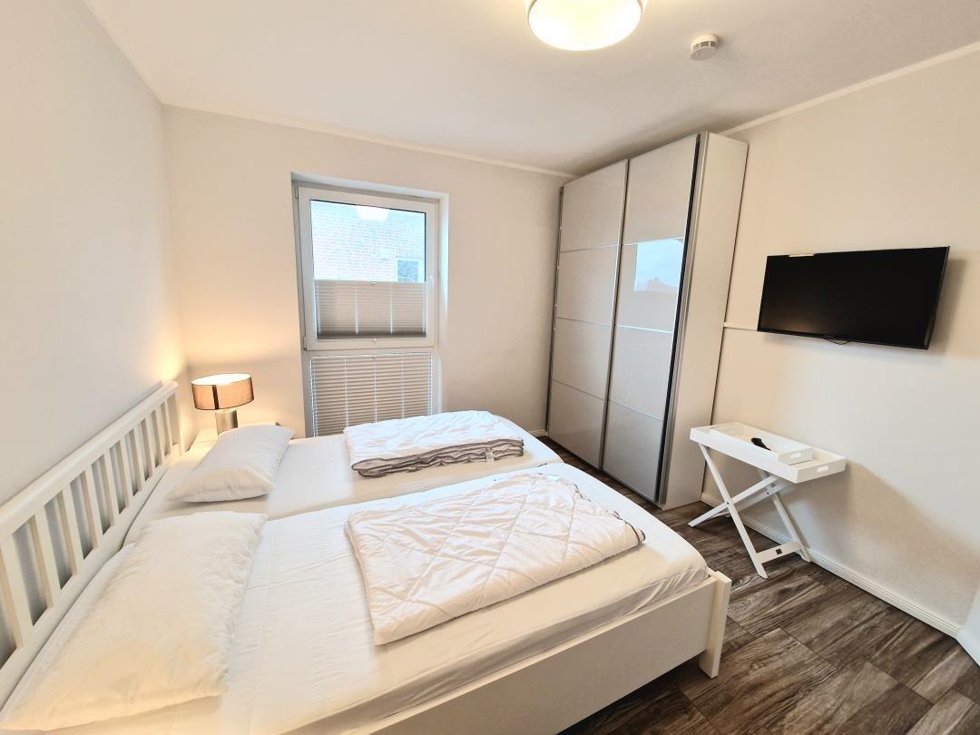 Schlafzimmer mit Doppelbett, Kleiderschrank, TV und Fenster.
